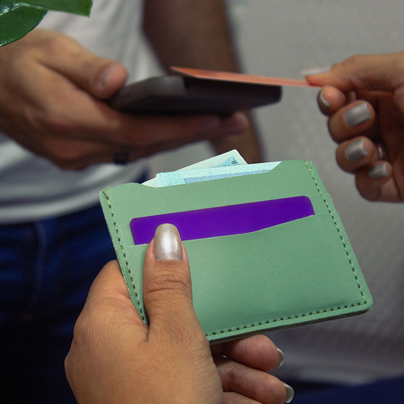 Uma carteira personalziada verde sendo segurada por uma mulher enquanto passa o cartão